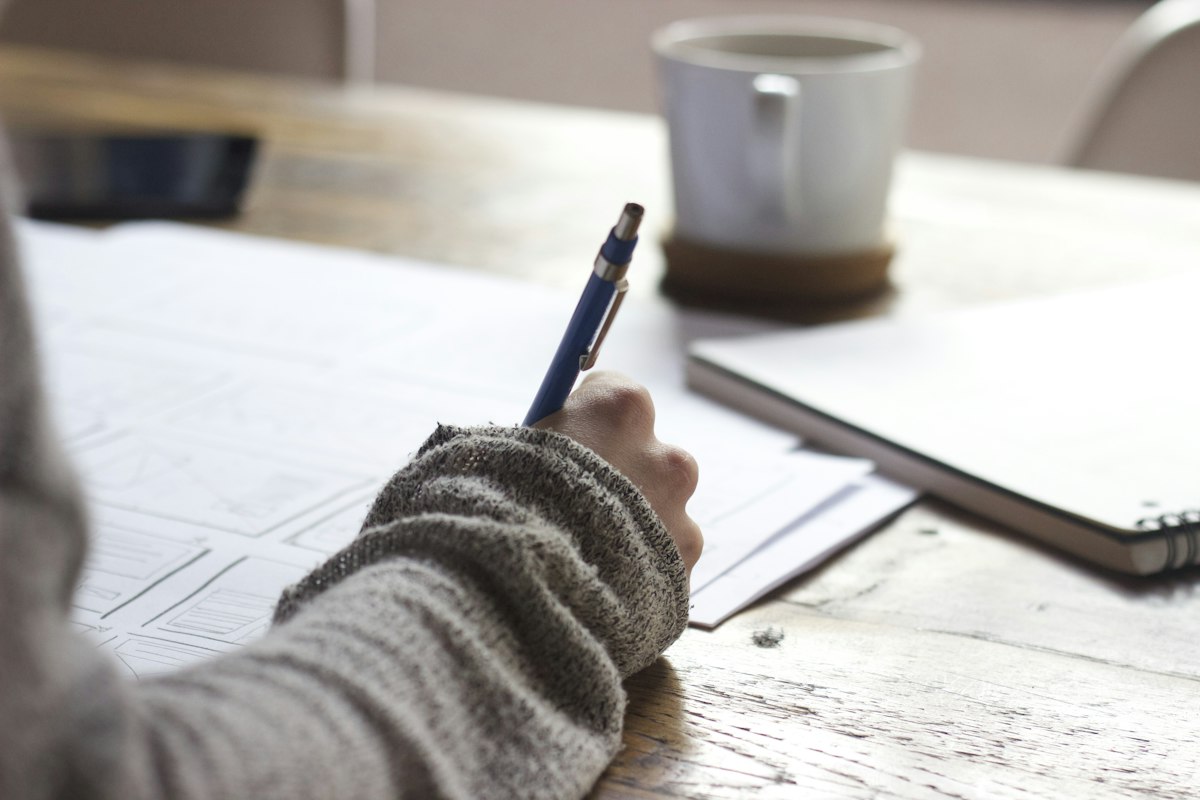 Person writing notes beside a cup of coffee